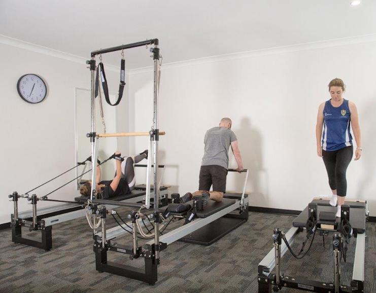 Man and a woman using pilates reformer machines for rehabilitation
